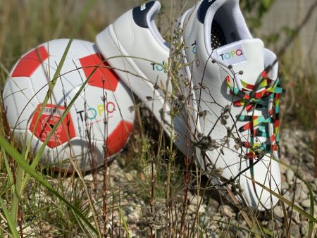 Białe buty sportowe i piłka z kolorowym logo TOPQ na tle trawy