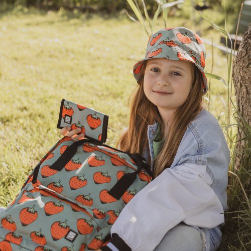 dziewczynka siedząca na trawie z plecakiem w arbuzy